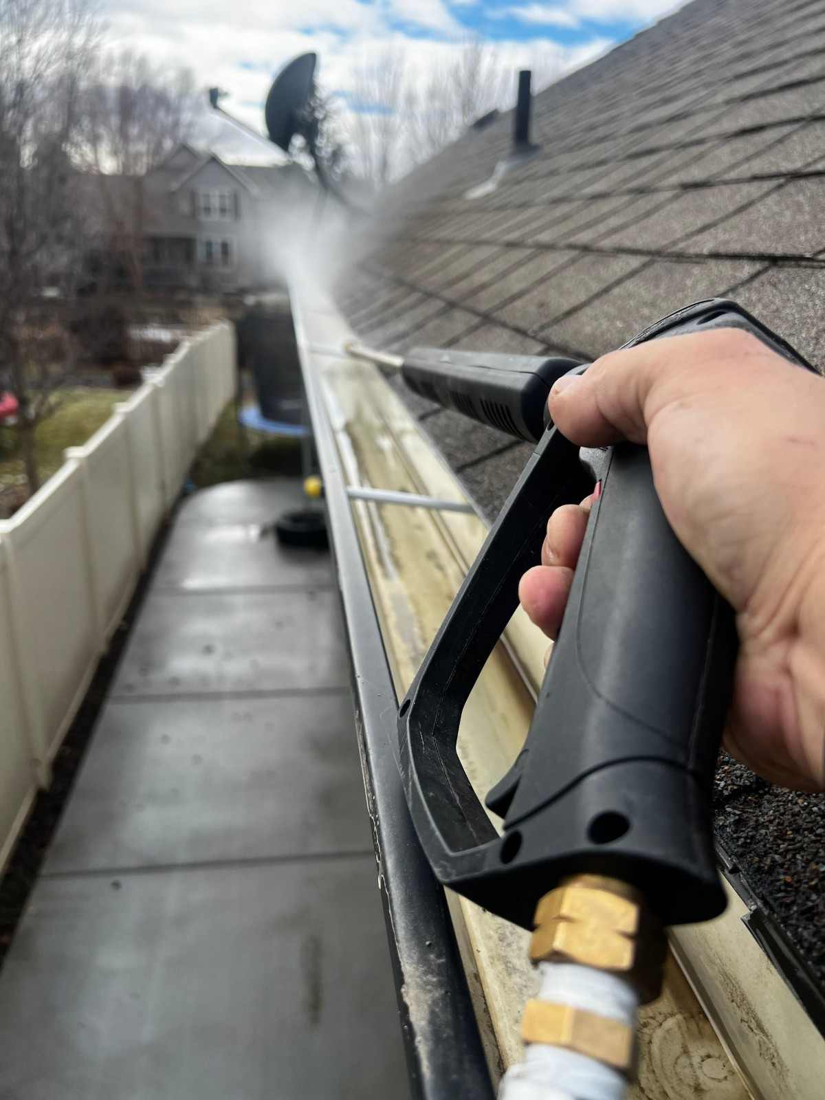 Close-up of gutter cleaning with pressure washer, outdoors, during the day.